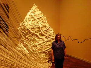 Pam Bowman stands next to "Becoming," the opening piece of the exhibit, which shows how small, everyday acts build up to create the whole of a person. (Photo by Mackenzie Brown)
