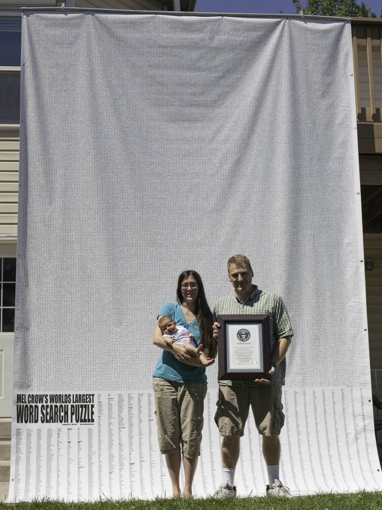 Mel Crow stands with his wife and child Malinda and Miley Crow in front of the world's largest word search puzzle he created.
