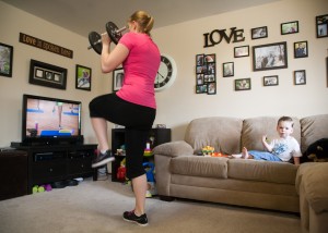 Kimberly Gardner works out in her Provo home while her child Porter plays with toys.