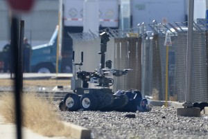 A bank robbery suspect wearing a motorcycle helmet lies handcuffed on the ground as a bomb squad robot searches his vest, Thursday, Jan. 22, 2015, in Salt Lake City. According to authorities, officers were struggling with the man as they tried to arrest him on suspicion of robbing a nearby bank when they noticed he was wearing a vest with wires. (AP Photo/The Salt Lake Tribune, Scott Sommerdorf)