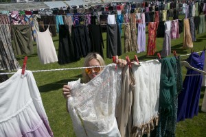 A woman hangs a dress among rows of women's clothing hanging, as a part of an art installation called 'Thinking of You' by Kosovo born artist Alketa Xhafa Mripa, in Pristina Stadium, Kosovo, Friday, June 12, 2015. Thousands of dresses and skirts were collected and hung across the field of the Pristina stadium, in a tribute to the estimated 20,000 wartime sexual violence survivors from Kosovo's 1998-1999 war for independence from Serbia. (AP Photo/Visar Kryeziu)