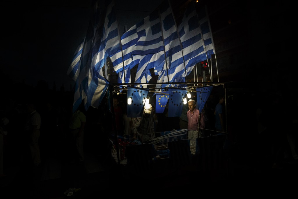 A man sells Greek and European Union flags during a rally organized by supporters of the YES vote for the upcoming referendum in front of the Greek Parliament in Athens, Tuesday, June 30, 2015. At midnight central Europe-time on Tuesday, the country is set to become the first developed nation to miss a debt repayment to the International Monetary Fund, as Greece sinks deeper into a financial emergency that has forced it put a nationwide lockdown on money withdrawals. (AP Photo/Daniel Ochoa de Olza)