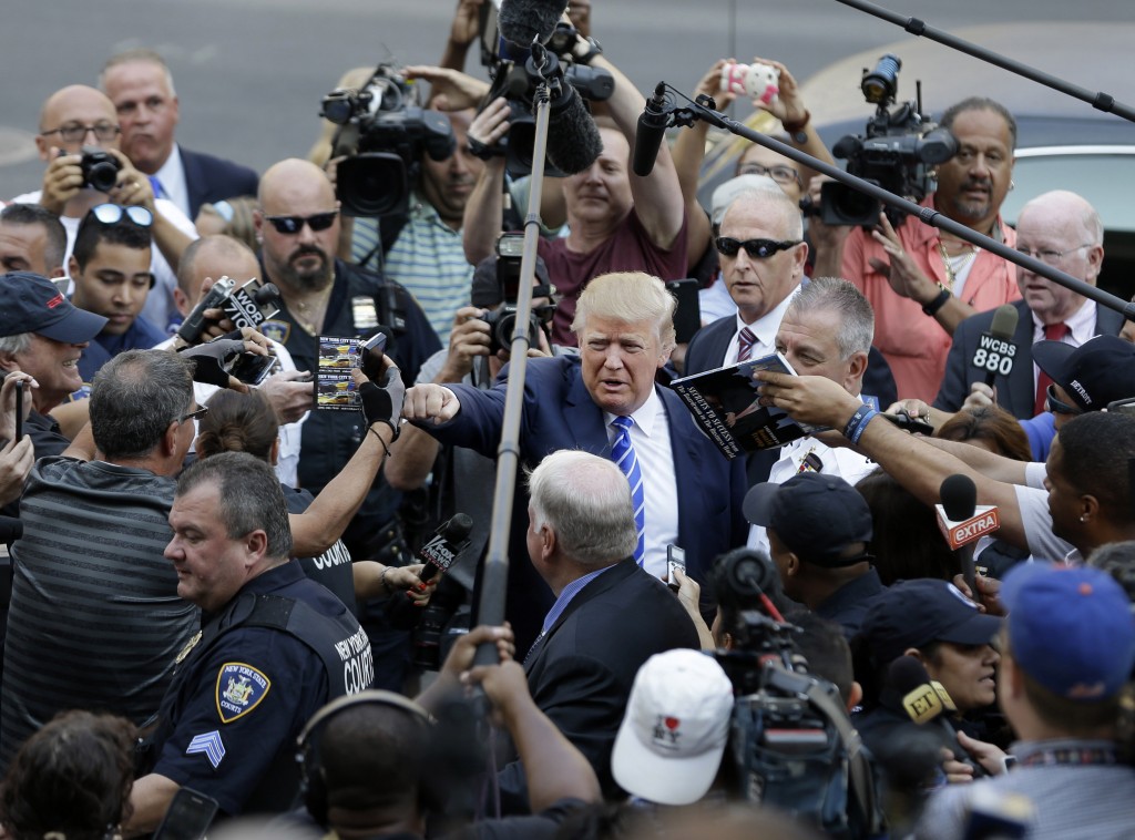 Donald Trump, center, gives a fist bump to a pedestrian as he arrives for jury duty in New York, Monday, Aug. 17, 2015. Trump was due to report for jury duty Monday in Manhattan.  (AP Photo/Seth Wenig)