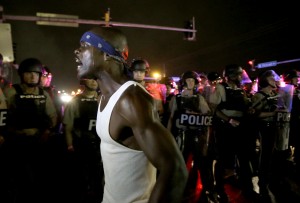 A protester yells as police form a line across West Florissant Ave., Sunday, Aug. 9, 2015, in Ferguson, Mo., before shots were fired near the protest. The one-year anniversary of Michael Brown's death in Ferguson began with a march in his honor and ended with a protest that was interrupted by gunfire. (AP Photo/Jeff Roberson)