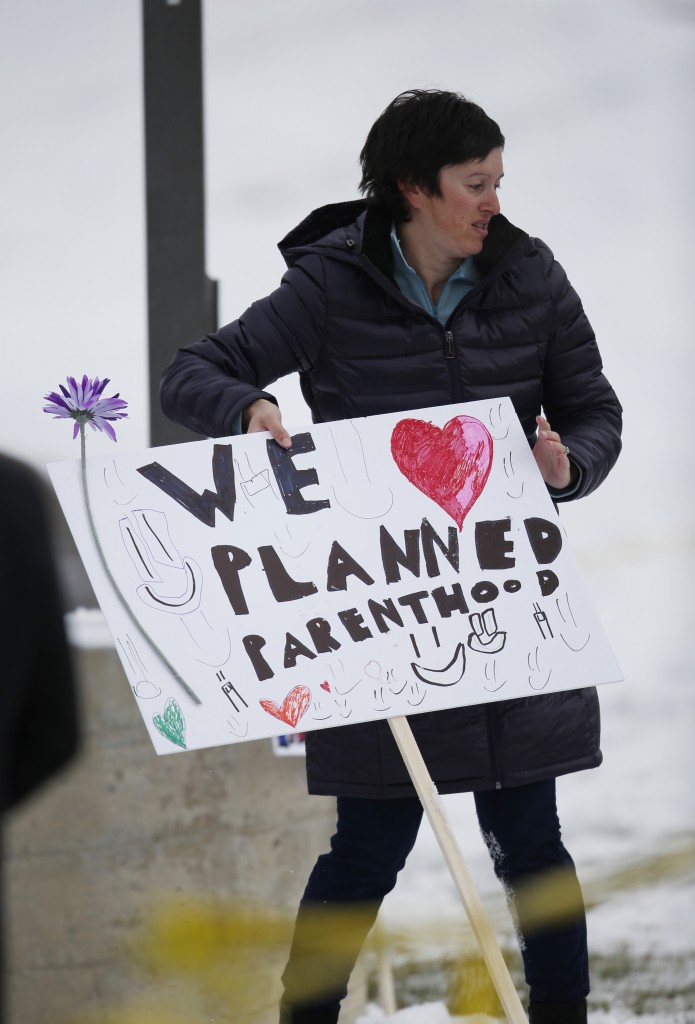 Bethany Winder, a nurse from Colorado Springs, Colo., plants a sign in support of Planned Parenthood south of the clinic as police investigators gather evidence near the scene of Friday's shooting at the clinic Sunday, Nov. 29, 2015, in northwest Colorado Springs. (AP Photo/David Zalubowski)